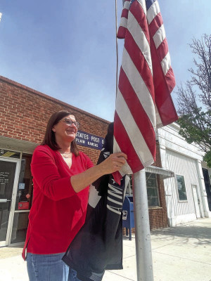 Dixie Selenke takes down the flags in front of the post office in Garden Plain. She retired on May 1 after a 15-year career with many stops in Sumner and Sedgwick counties. Travis Mounts/TSnews