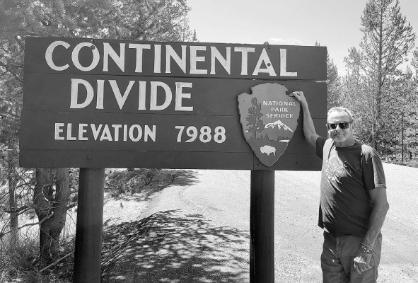 Publisher Paul Rhodes stands by a Continental Divide marker in the heart of Yellowstone National Park. Contributed photo/Kim Swansen
