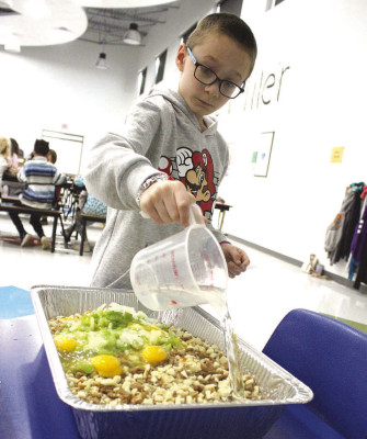 Rylan Adams pours water into stuffing last week. Students at Oak Street Elementary play active roles in preparing their annual school Thanksgiving feast. Travis Mounts/TSnews