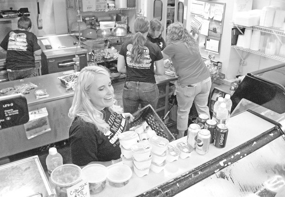 Jenny Osner, co-owner of Hired Man’s Grocery &amp; Grill, visits with customers during Saturday’s 15th anniversary celebration. Store employees and volunteers, including Mary Hoisington of Wheatland Electric, help prepare the free hot dogs that were served.